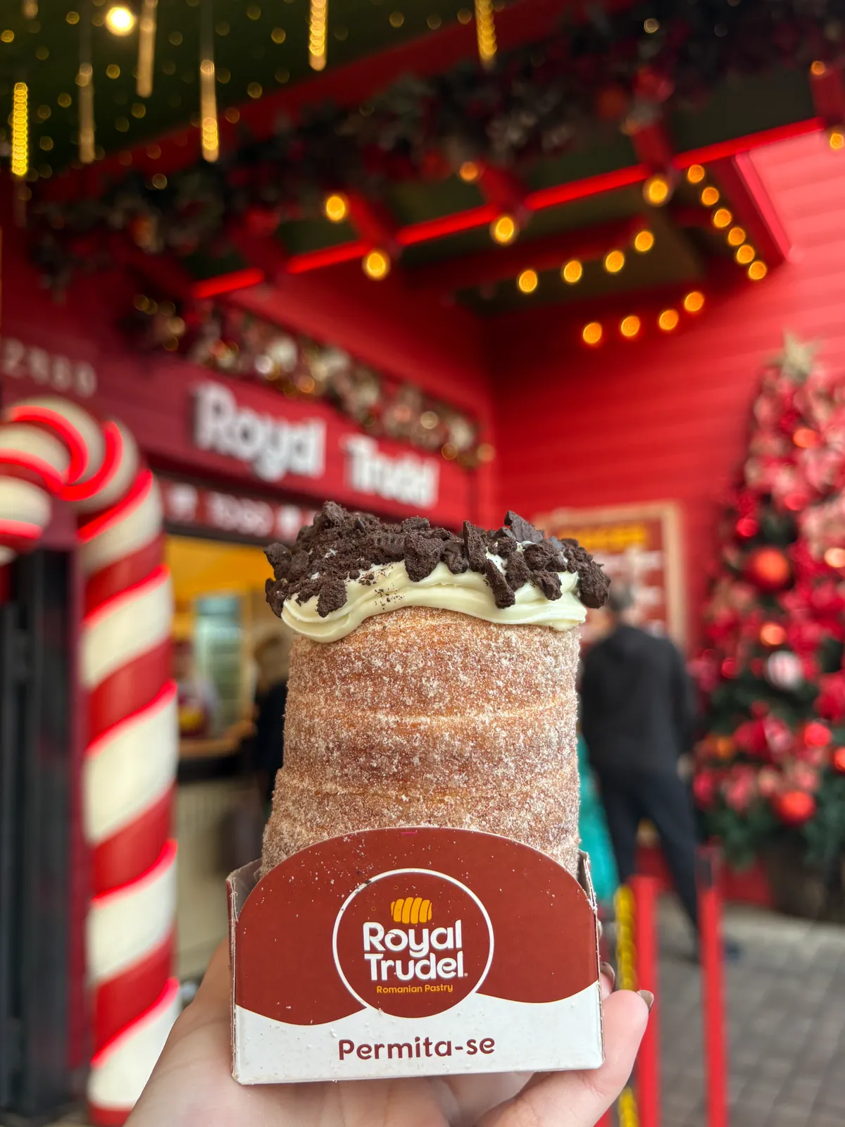 Trudel com cobertura de creme e biscoito, em embalagem Royal Trudel, diante de uma loja decorada para o Natal